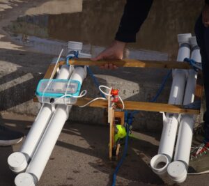 A photo of the model turbine mounted on a raft made from domestic drain pipes and wood with the electronics mounted on it.