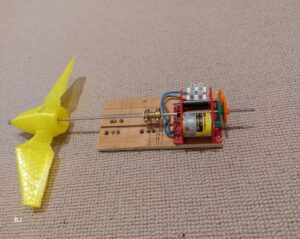 An image of the turbine showing a 3d printed blade and a generator with gearing all mounted on a wooden board.